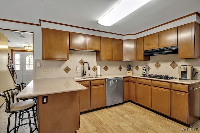 kitchen with a breakfast bar, under cabinet range hood, a sink, stainless steel appliances, and a peninsula