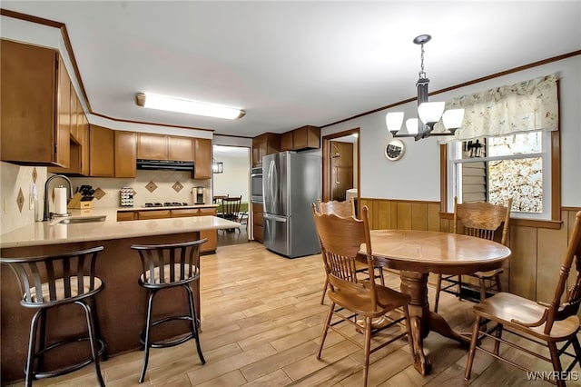 dining room featuring ornamental molding, wooden walls, light wood-style floors, an inviting chandelier, and wainscoting