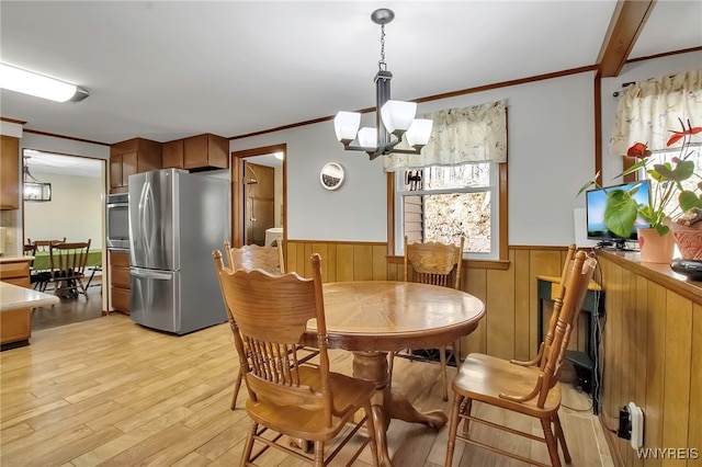 dining space featuring a wainscoted wall, a notable chandelier, crown molding, and light wood finished floors