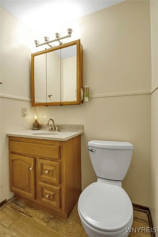 half bathroom with a wainscoted wall, toilet, vanity, and a decorative wall