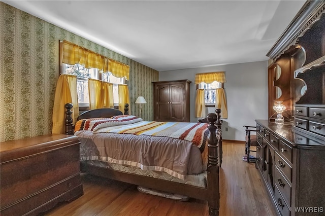 bedroom with baseboards, wood finished floors, and wallpapered walls