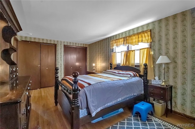 bedroom featuring two closets, wood finished floors, and wallpapered walls