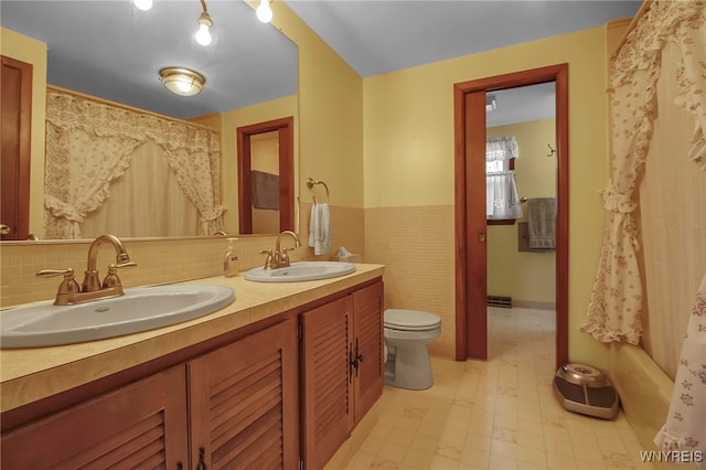 full bath with a sink, toilet, double vanity, and wainscoting