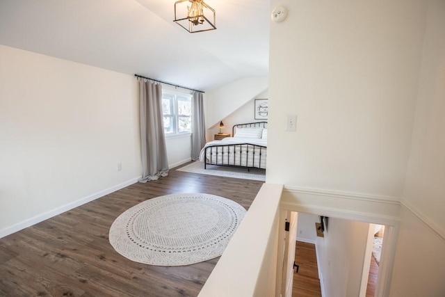 bedroom featuring lofted ceiling, a notable chandelier, wood finished floors, and baseboards