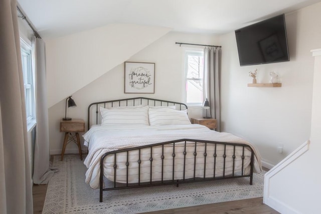 bedroom with baseboards, lofted ceiling, and wood finished floors