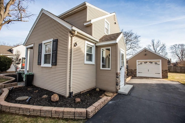 view of property exterior featuring a detached garage, an outdoor structure, fence, and driveway