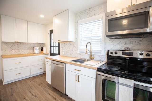 kitchen featuring butcher block counters, appliances with stainless steel finishes, light wood-style floors, white cabinetry, and a sink