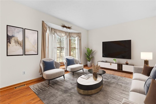 living area with visible vents, baseboards, wood finished floors, and vaulted ceiling