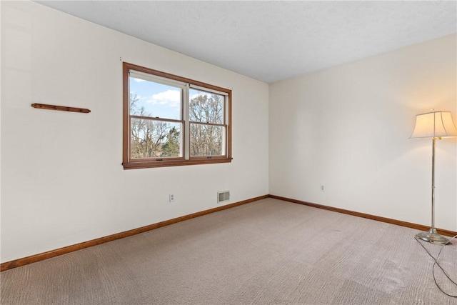 spare room featuring light colored carpet, visible vents, and baseboards