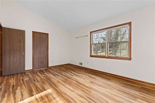 unfurnished bedroom with vaulted ceiling, wood finished floors, visible vents, and baseboards