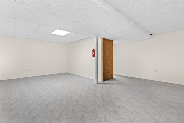 finished below grade area featuring tile patterned floors, a paneled ceiling, and baseboards