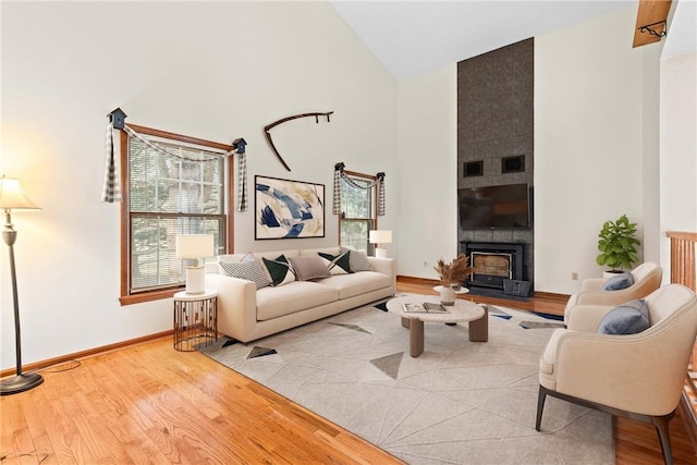 living room featuring a large fireplace, wood finished floors, baseboards, and high vaulted ceiling