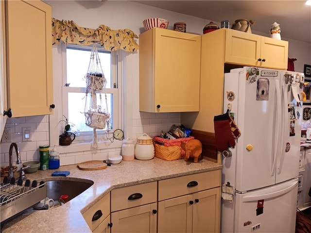 kitchen with tasteful backsplash, freestanding refrigerator, light stone counters, and a sink