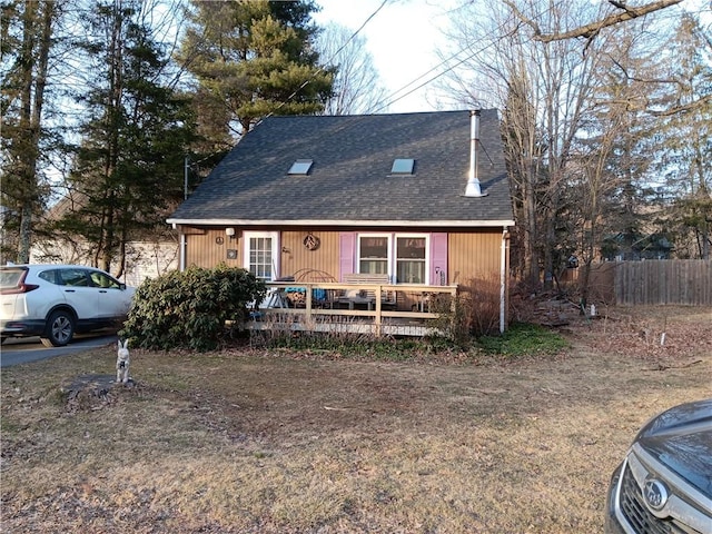 view of front of property with roof with shingles, a deck, and fence