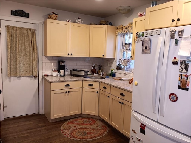 kitchen featuring dark wood-type flooring, a sink, light stone counters, tasteful backsplash, and freestanding refrigerator