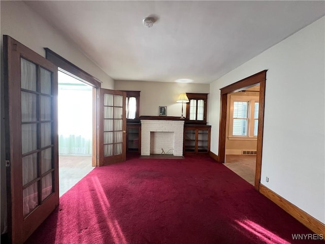 unfurnished living room with a wealth of natural light, visible vents, a brick fireplace, and carpet