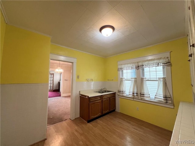 kitchen featuring a notable chandelier, a sink, crown molding, light wood finished floors, and light countertops