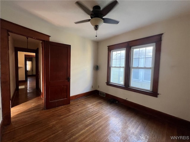 spare room featuring visible vents, a ceiling fan, dark wood-type flooring, and baseboards