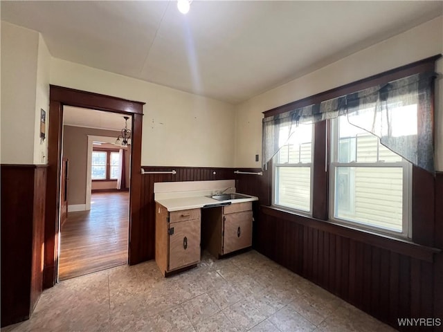 kitchen with a sink, wood walls, wainscoting, and light countertops