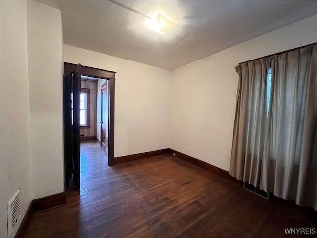 spare room featuring dark wood-style floors, visible vents, and baseboards