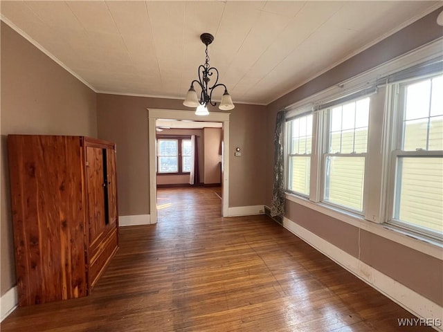 unfurnished dining area with hardwood / wood-style floors, crown molding, a notable chandelier, and baseboards