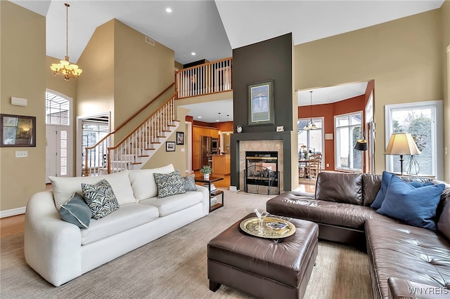 living room with a tiled fireplace, a high ceiling, baseboards, a chandelier, and stairs