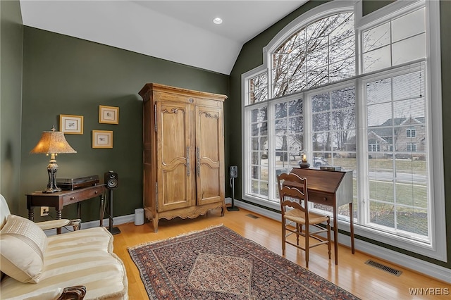 office space featuring vaulted ceiling, light wood-style floors, visible vents, and baseboards