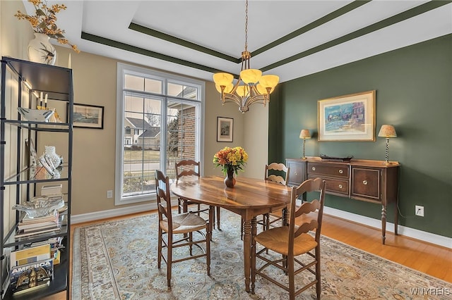 dining space with an inviting chandelier, a tray ceiling, light wood-style flooring, and baseboards