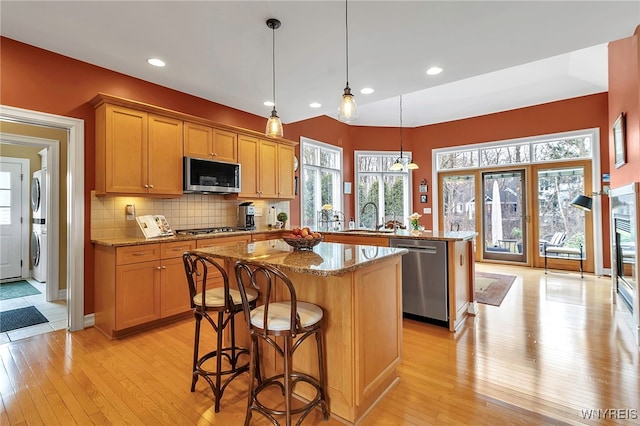 kitchen with a kitchen island, a peninsula, a sink, appliances with stainless steel finishes, and backsplash