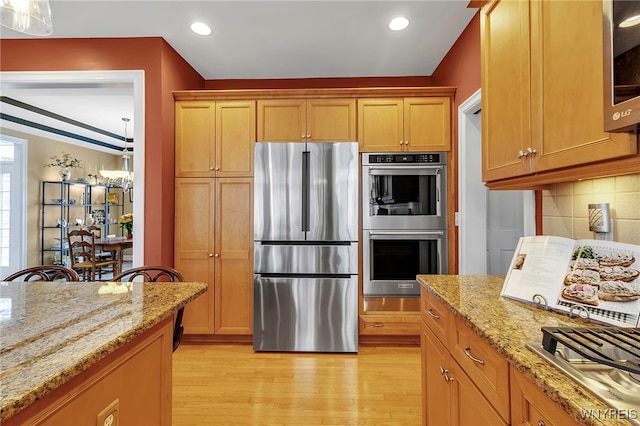 kitchen with light stone counters, recessed lighting, appliances with stainless steel finishes, light wood finished floors, and decorative backsplash