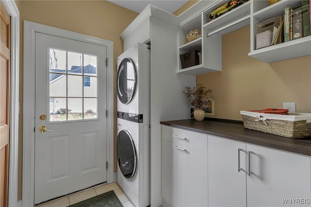 clothes washing area featuring light tile patterned floors, stacked washer / dryer, and cabinet space