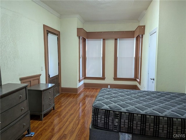 bedroom featuring ornamental molding, a textured ceiling, wood finished floors, baseboards, and a textured wall