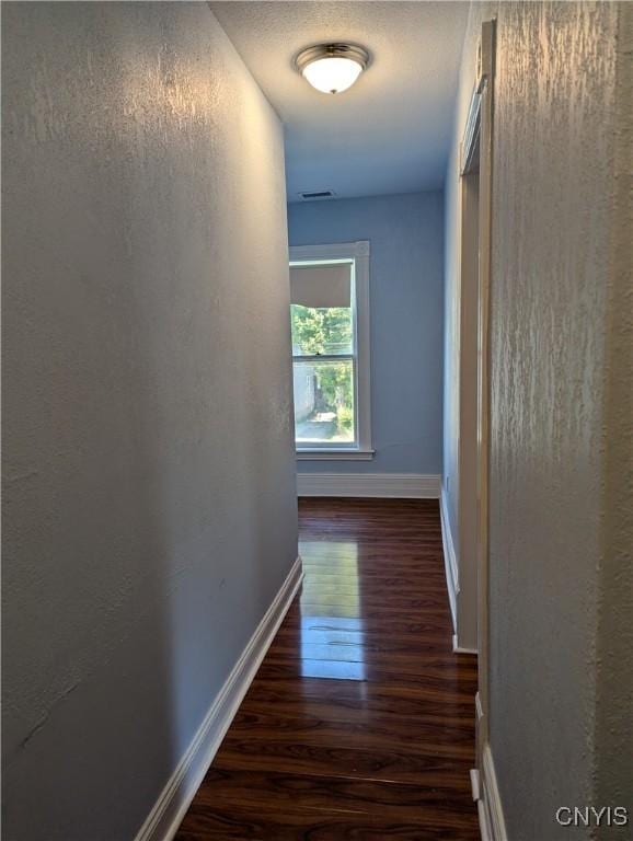 hall with visible vents, baseboards, dark wood finished floors, a textured ceiling, and a textured wall