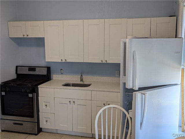 kitchen with a sink, white cabinetry, freestanding refrigerator, light countertops, and stainless steel gas range