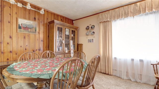 dining room featuring light colored carpet, wood walls, and ornamental molding