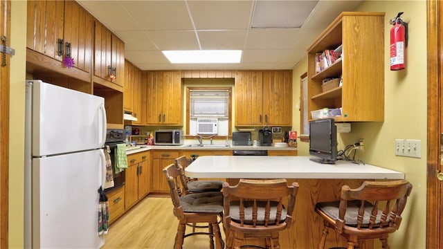 kitchen with light wood finished floors, light countertops, a peninsula, black appliances, and open shelves