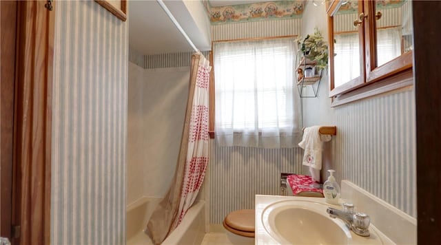 bathroom with a sink, toilet, shower / bath combo, and wallpapered walls