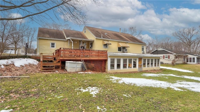 snow covered back of property featuring a lawn, a deck, and a sunroom