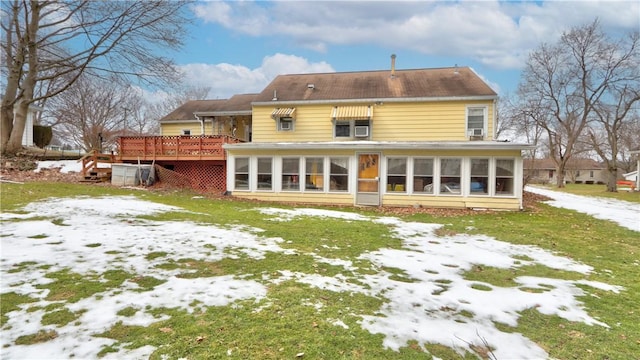 snow covered back of property with a wooden deck, a yard, and a sunroom