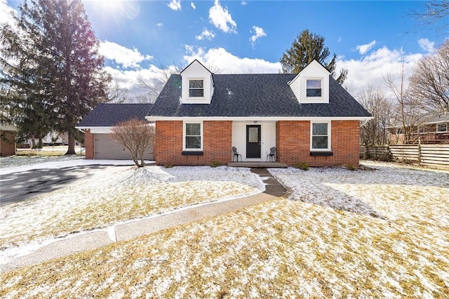 cape cod house with brick siding, an attached garage, driveway, and fence