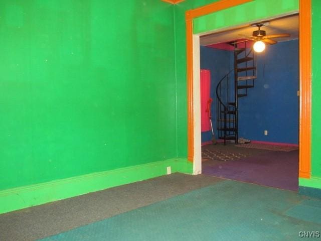 carpeted spare room featuring stairs and a ceiling fan