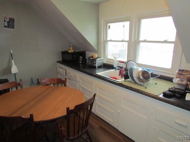 kitchen featuring dark countertops, black microwave, dark wood-style floors, white cabinets, and a sink