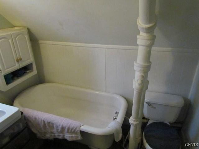 full bathroom featuring toilet, a tub to relax in, and wainscoting