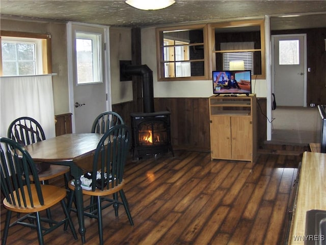 dining room featuring a wainscoted wall, dark wood-type flooring, and a wood stove