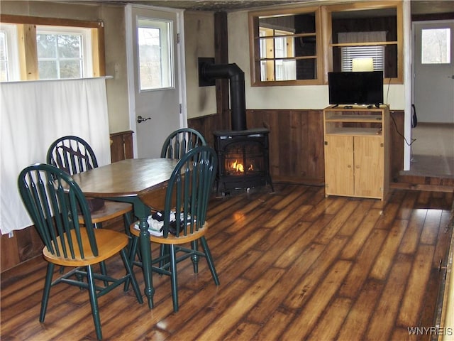 dining area with dark wood-style floors, wainscoting, and a wood stove