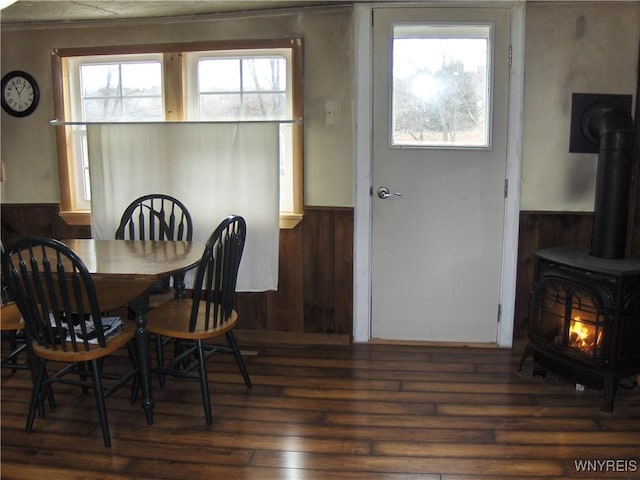 dining room with wainscoting, a wood stove, wood walls, and wood finished floors