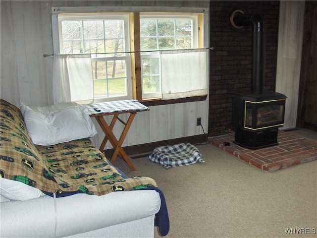 living area featuring a wealth of natural light, wooden walls, carpet, and a wood stove