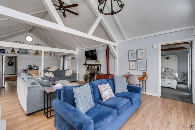 living area featuring light wood-type flooring, beamed ceiling, a stone fireplace, baseboards, and ceiling fan