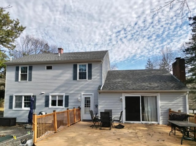 back of house with a deck, outdoor dining area, a shingled roof, and a chimney