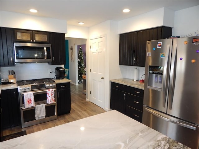 kitchen featuring backsplash, recessed lighting, appliances with stainless steel finishes, light wood finished floors, and dark cabinets